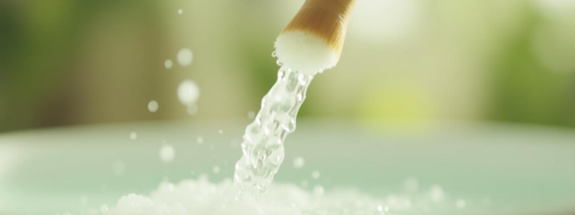 Close-up of makeup being gently cleansed from a brush with a natural cleaning solution, water softly streaming to purify.